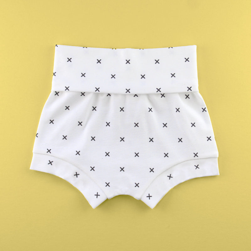 Fold over baby bummie shorts in an x fabric on a yellow background