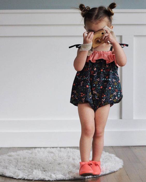 Toddler Girl in Black Floral Tie Strap Romper Holding a Wooden Camera