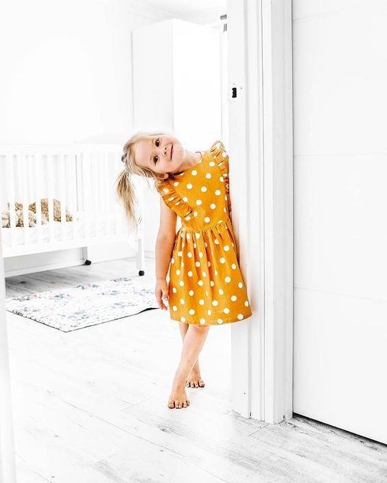 Toddler Girl in Bright Yellow Polka Dot Ruffle Dress Standing in White Room
